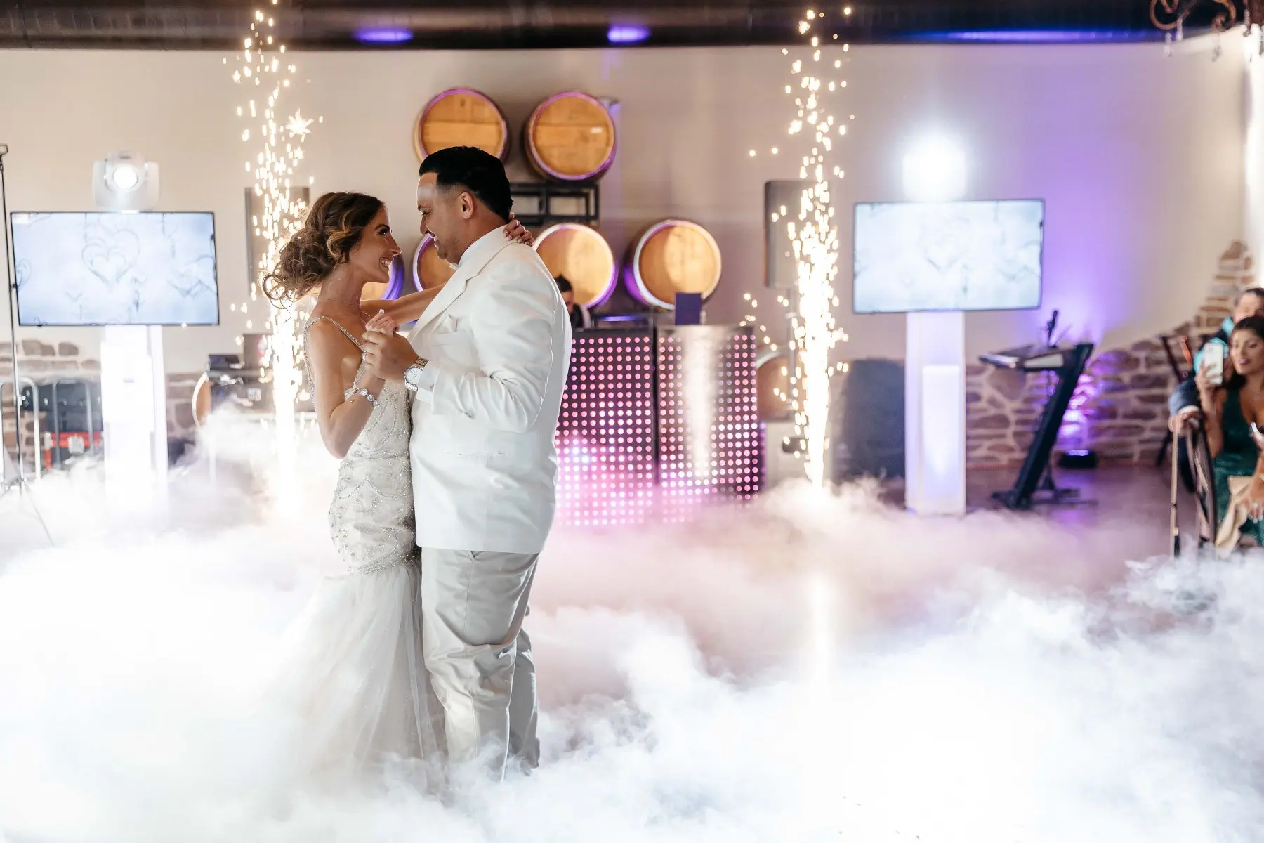 Novios sonriendo durante su primer baile entre nubes y chispas frías